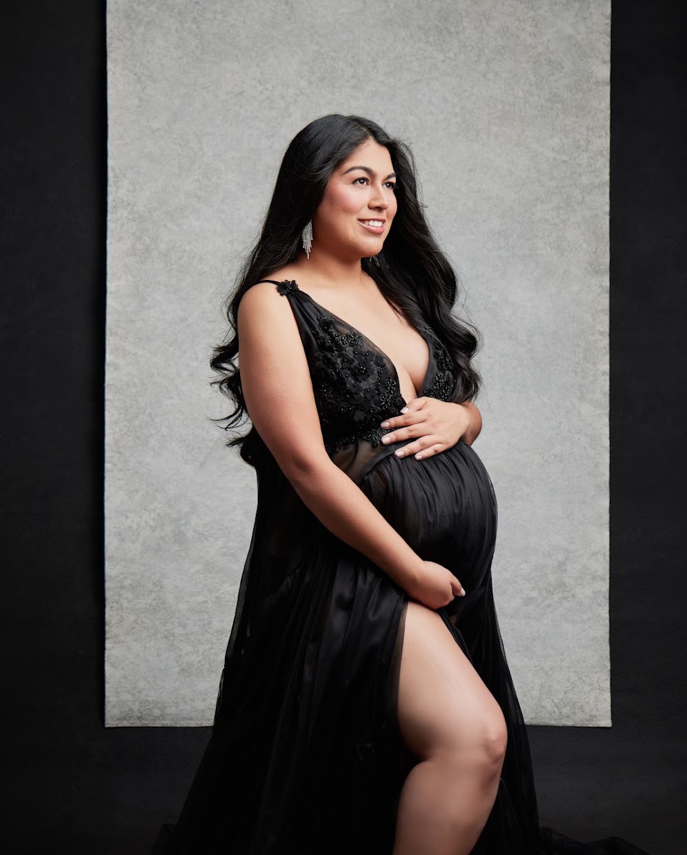 Dr. Crystal Corona smiling in a black maternity gown, holding her pregnant belly